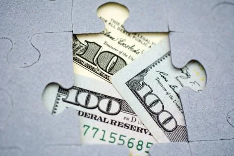 Hundred dollar bills through the missing piece of jigsaw puzzles. Business an Stock Photos