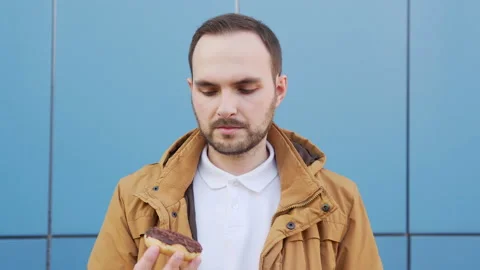Hungry bearded man sniffs a chocolate donut and admires its aroma. Stock Footage 137860696