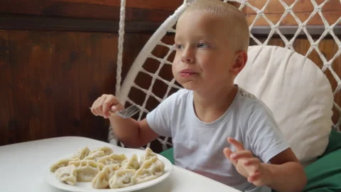 Hungry Boy Chewing Delicious Dumplings With Appetite In Hanging Chair Stock Footage 321677901