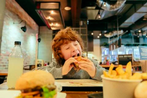 Hungry boy eats burger in restaurant Stock Photos