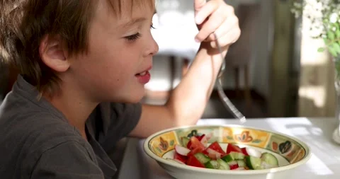 Hungry boy eats vegetable salad at table in country house Stock Footage 263696467