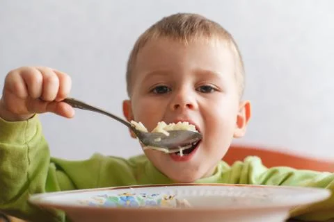 Hungry child eats lunch with big appetite. Cute boy eats pasta. Stock Photos