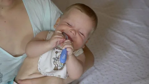 A hungry cute infant sitting on her mother’s arms licks a baby spoon Stock Footage 138507152