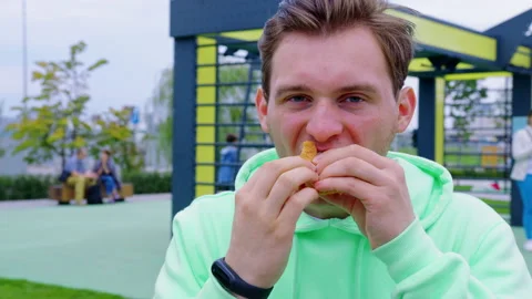 Hungry guy bites off, chews sandwich in the city park Stock Footage 196334953