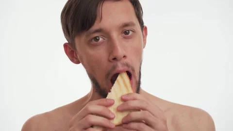 Hungry half naked man with beard eat sandwich in slow motion on white background Video stock 147612588