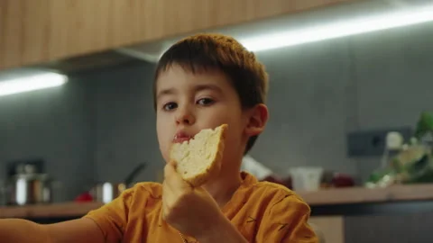 Hungry kid boy eating a slice of white sitting on chair in kitchen, having lunch Stock Footage 269889126