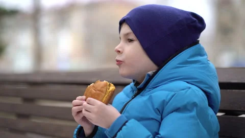 Hungry kid eating double cheeseburger outdoor Stock Footage 152110196