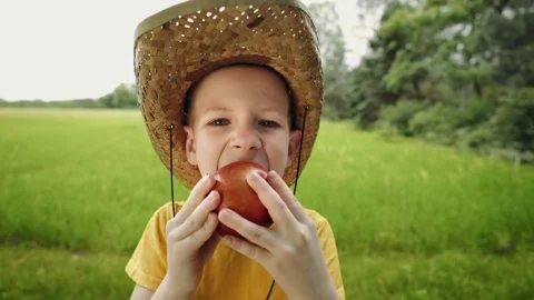 Hungry kid eats an apple with great pleasure. Portrait of a guy in a straw hat Stock-Footage 165740983