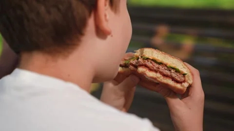 Hungry little boy taking bite of hamburger, kid holding big burger with sesame b Video stock 334855617