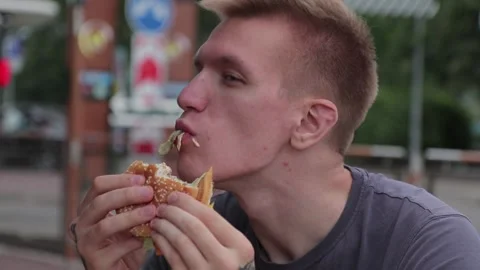 Hungry man appetizingly chews a burger after workout in the street 스톡 동영상 149266633
