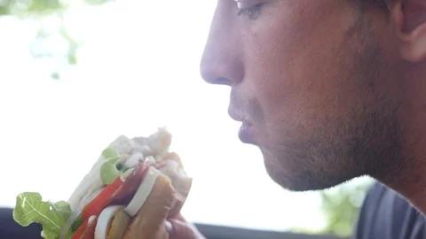 A hungry man with a big appetite bites a hearty hamburger. HD, 1920x1080, slow Stock Footage 95940242