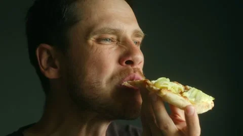 Hungry man eating pizza slice with enthusiasm on dark background Stock Footage 311754155