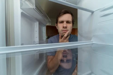 Hungry man is looking for food in empty fridge. Stock Photos