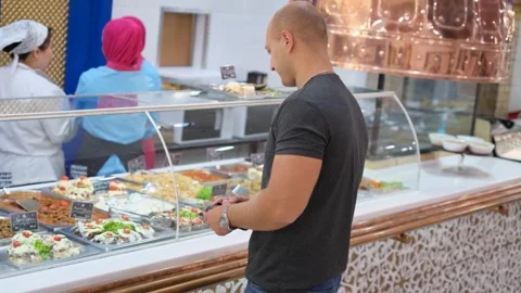 Hungry man looking at showcase with ready meals in mall diner Stock Footage 248789809