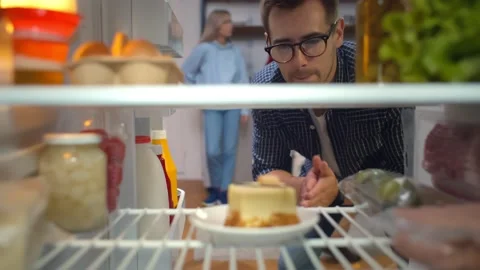 Hungry man looking for a snack in fridge taking piece of cake Stock Footage 139222041