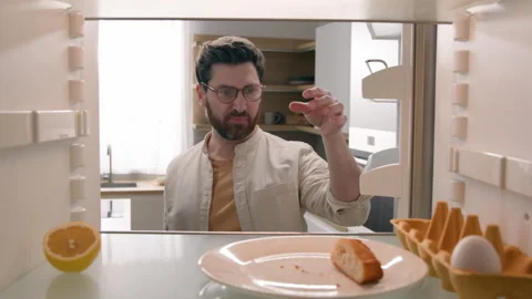 Hungry man open empty refrigerator with half lemon, lettuce leaf, one egg, slice Stock Footage 244520111