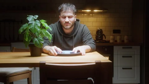 Hungry man sitting at kitchen table waiting for food with empty plate and c.. Stock Footage 307491626