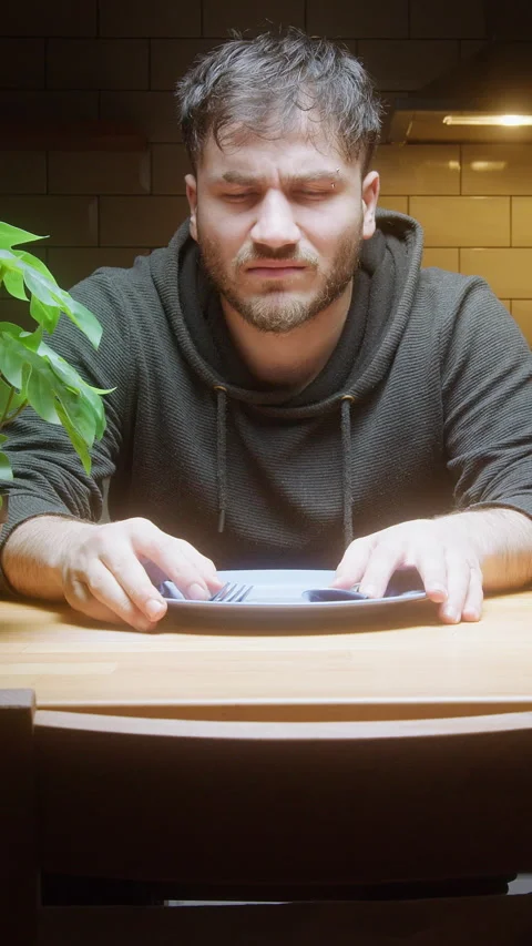 Hungry man sitting at kitchen table waiting for food with empty plate and c.. Video stock 307516677