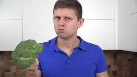 Hungry, sad man in the kitchen eating raw broccoli. A portrait of a man who Stock Footage 150379498