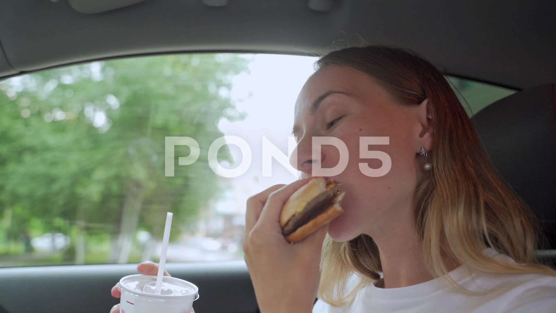 Hungry woman eating burger sitting in car, junk food