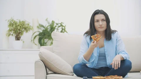 Hungry woman is switching on the TV program, while sitting on a sofa. She is Stock Footage 120884907