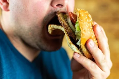 The hungry young man aggressively eats a burger. Fast food Stock Photos