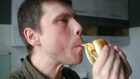 Hungry young man greedily biting into a juicy cheeseburger Stock Footage 337830504