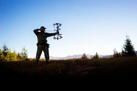 Hunter aiming with bow and arrow while standing against clear sky Stock Photos