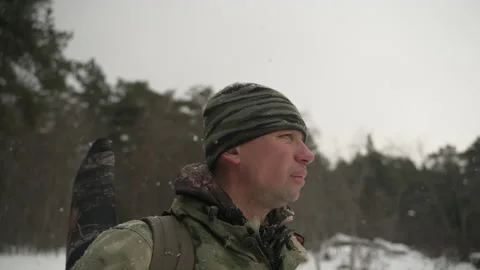 A hunter with a backpack and a gun behind his back looks around in the winter Stockbeeldmateriaal 169097858