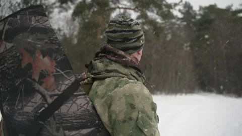 A hunter with a backpack and a gun behind his back looks around in the winter Vidéo 169302126