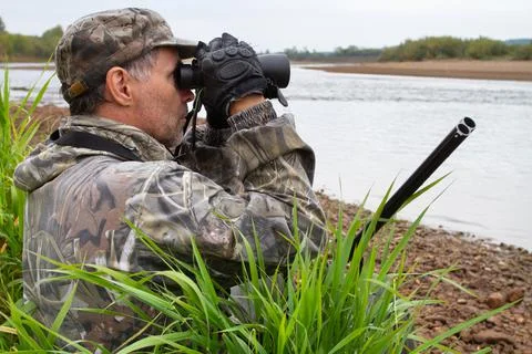 A hunter examines the coast of the river with binoculars Stock Photos