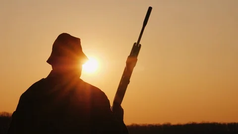 A hunter with a gun goes forward across the field towards the setting sun. Hobby Stock Footage 106023935