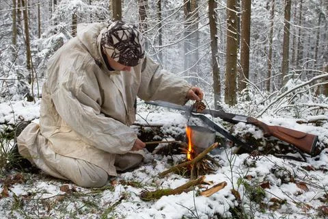 A hunter hangs a pot over a fire in a winter forest Stock Photos