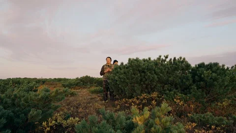Hunter hides behind a cedar bush shows his hand into the distance Stock Footage 117396447