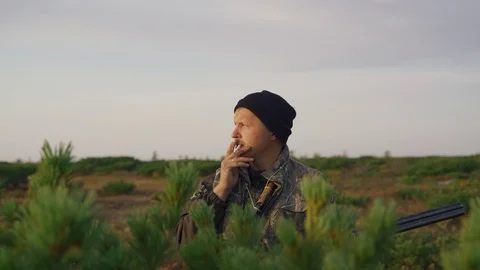 Hunter hides behind a cedar bush smokes Stock Footage 117398297