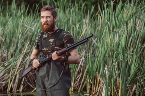 Hunter holding rifle while looking away on grassy field Stock Photos