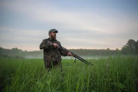 Hunter holding rifle while standing on field against sky Stock Photos