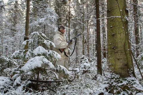 A hunter holds a shotgun in his hands in the winter twilight forest Stock Photos
