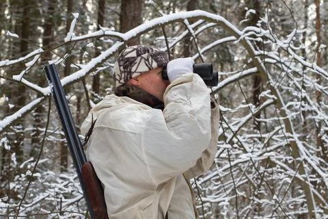 A hunter looks through binoculars in the forest during a winter hunt Stock Photos