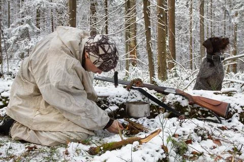 Hunter makes a fire in a snowcovered forest Stock Photos