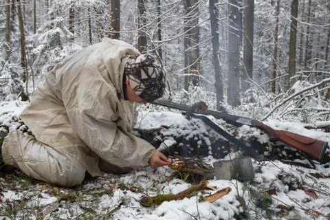 A hunter makes a fire in the winter forest Stock Photos
