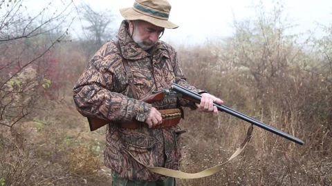 Hunter man with gray beard in hunter suit load cartridges in a double-barreled r Video stock 164292890
