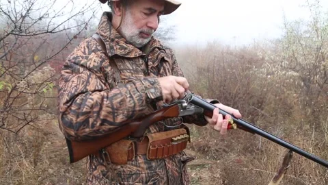 Hunter man with gray beard in hunter suit load cartridges in a double-barreled r Video stock 164292944