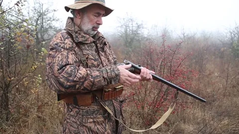 Hunter man with gray beard in hunter suit load cartridges in a double-barreled r Stock Footage 164293411