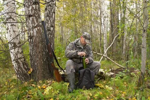 Hunter opens a thermos of tea while resting on a fallen tree Stock Photos
