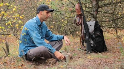Hunter resting in forest. drinking tea. shotgun, ammunition on the background 스톡 동영상 97781744