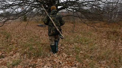 Hunter with rifle in the forest. Rest time under the big tree Stock Footage 100630786