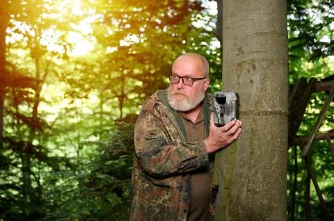 Hunter sets a trail camera on a tree in the forest. Trail cameras are often.. Stock Photos