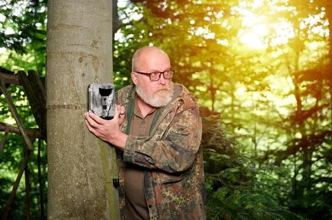 Hunter sets a trail camera on a tree in the forest. Trail cameras are often.. Stock Photos