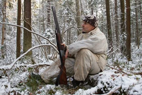 A hunter sits on a fallen tree in a winter forest Stock Photos